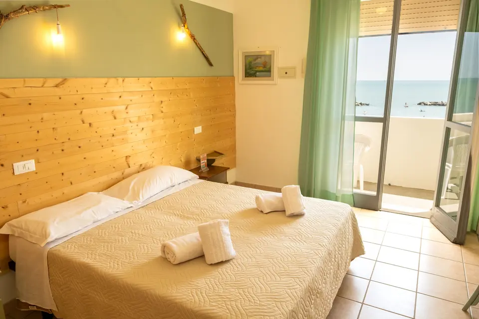 Ahşap başlıklı aydınlık çift kişilik oda ve denize açılan balkon kapısı